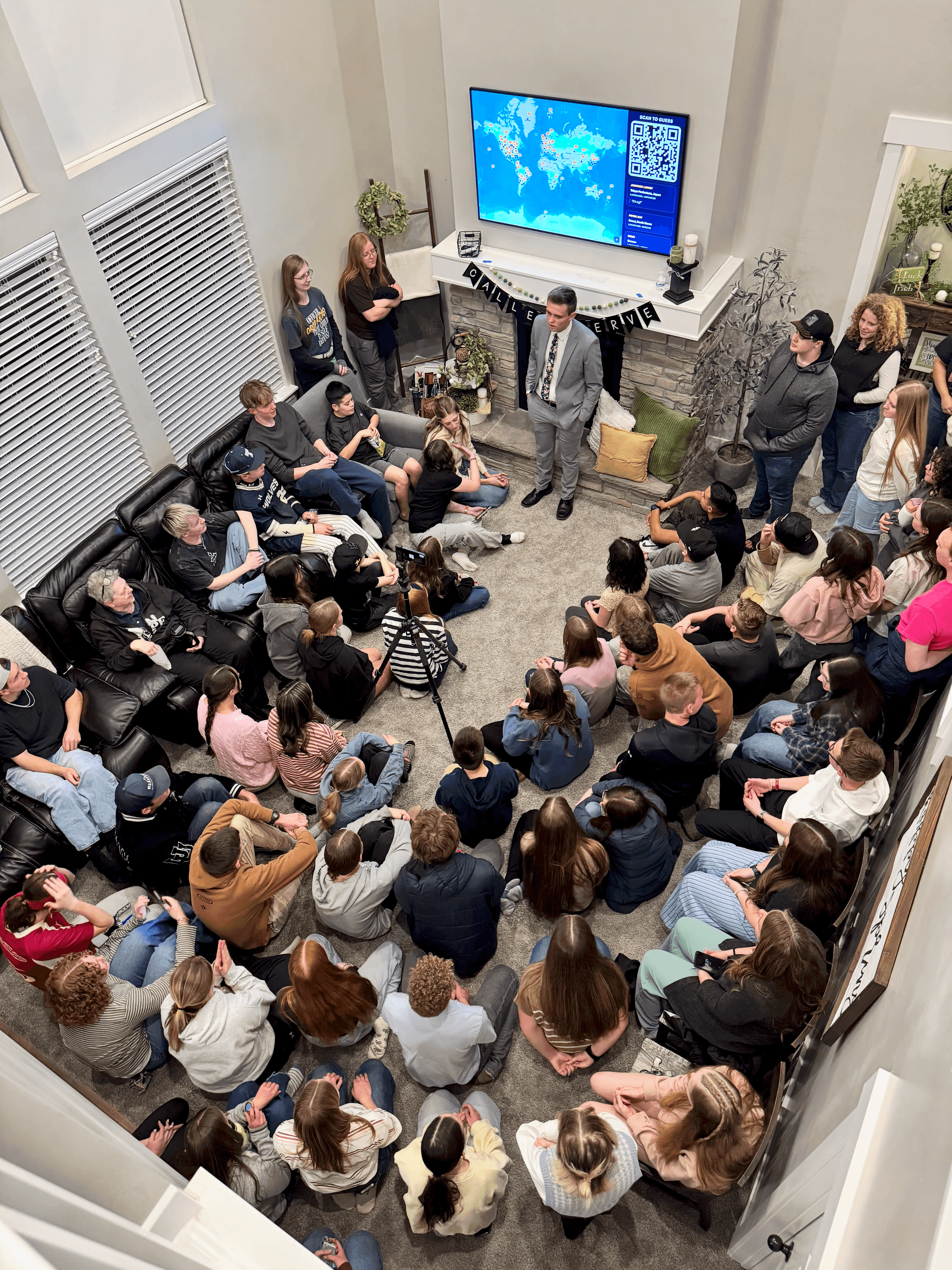 A mission call opening gathered around a large display showing the live Mission Call Guesser map.